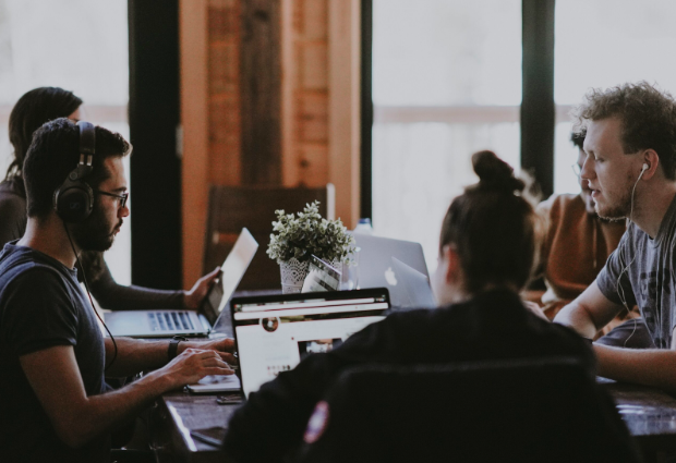 five people sit around a table with laptops in front of them discussing SEO